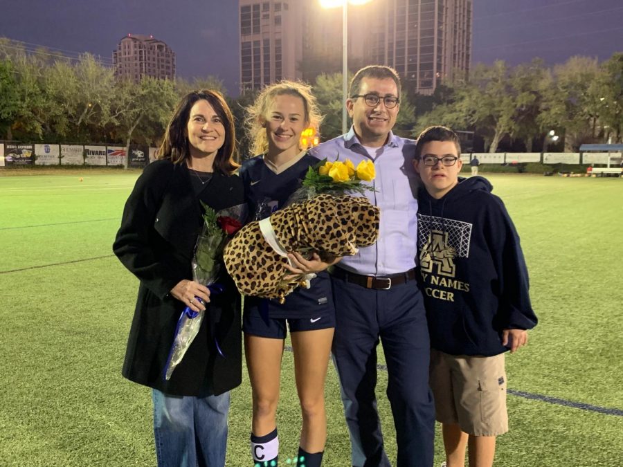 Senior team captain Olivia Tremonti holds awards from her senior night: yellow roses and a jaguar blanket, alongside her parents and younger brother Michael. 