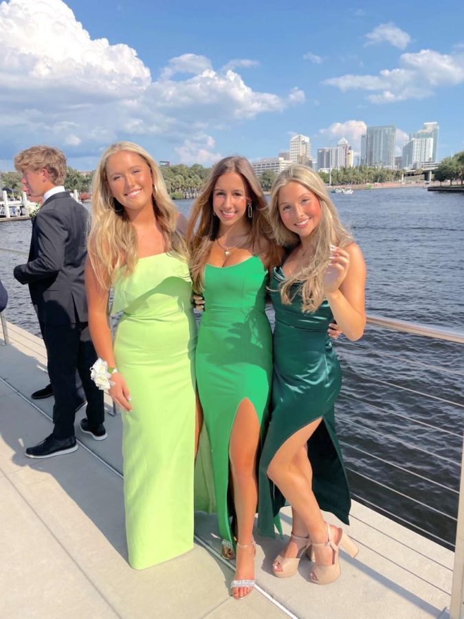 Juniors, Smith Cassidy, Maggie Smith, and Ava Politz posing in their green dresses in front of Riverwalk.
